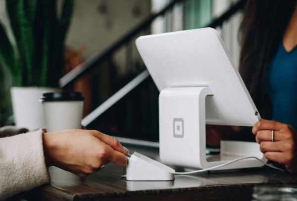 O persoană introduce un card de credit pe un terminal de plată fără fir la un ghișeu, cu un sistem modern de punct de vânzare și o ceașcă de cafea to-go în fundal.