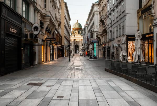 O stradă goală pietruită, străjuită de magazine de lux și cafenele, care duce la o clădire istorică în formă de cupolă în fundal, în lumina dimineții timpurii.