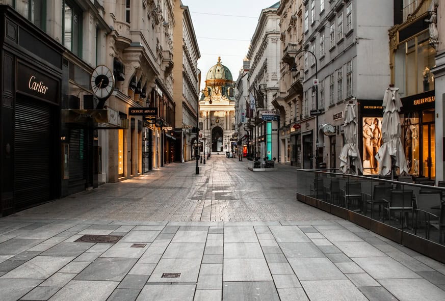 O stradă goală pietruită, străjuită de magazine de lux și cafenele, care duce la o clădire istorică în formă de cupolă în fundal, în lumina dimineții timpurii.